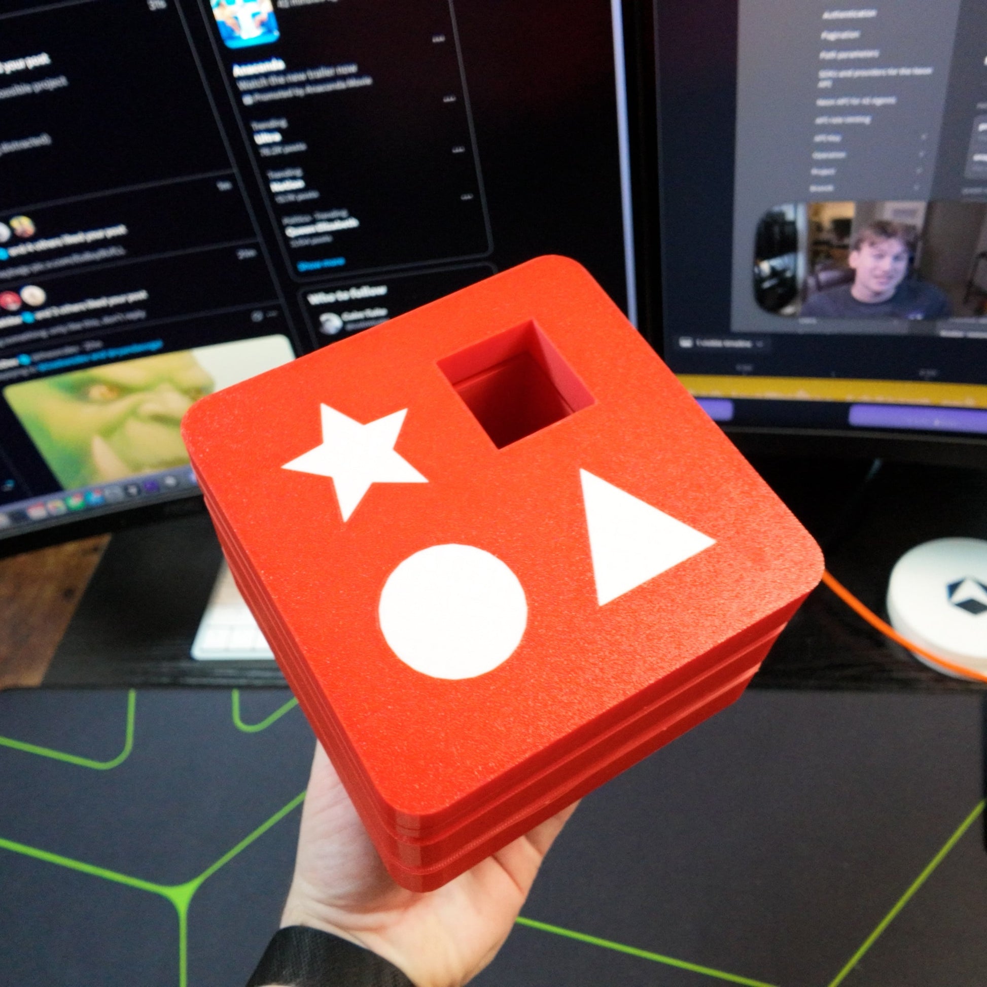 Red block with white stars and circles held in front of computer monitors displaying a video call.